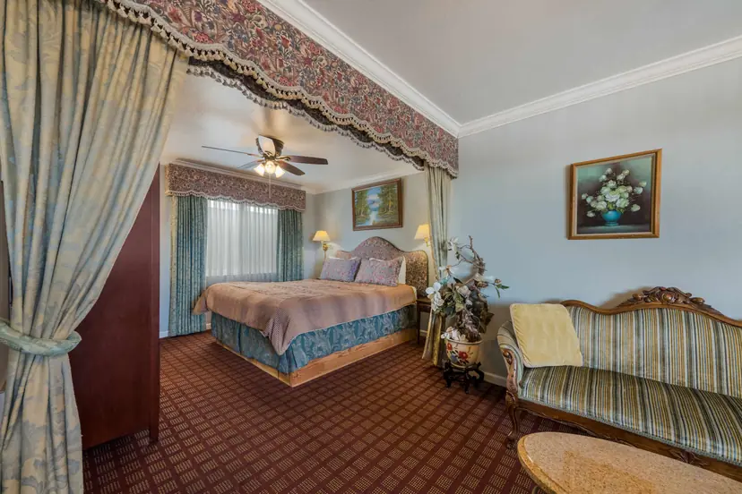 King suite at Carmel Inn & Suites with the bed in a draped alcove under a floral valance, and a striped antique settee