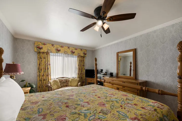 Standard King room with a king bed, ceiling fan, dresser and armchair by the window